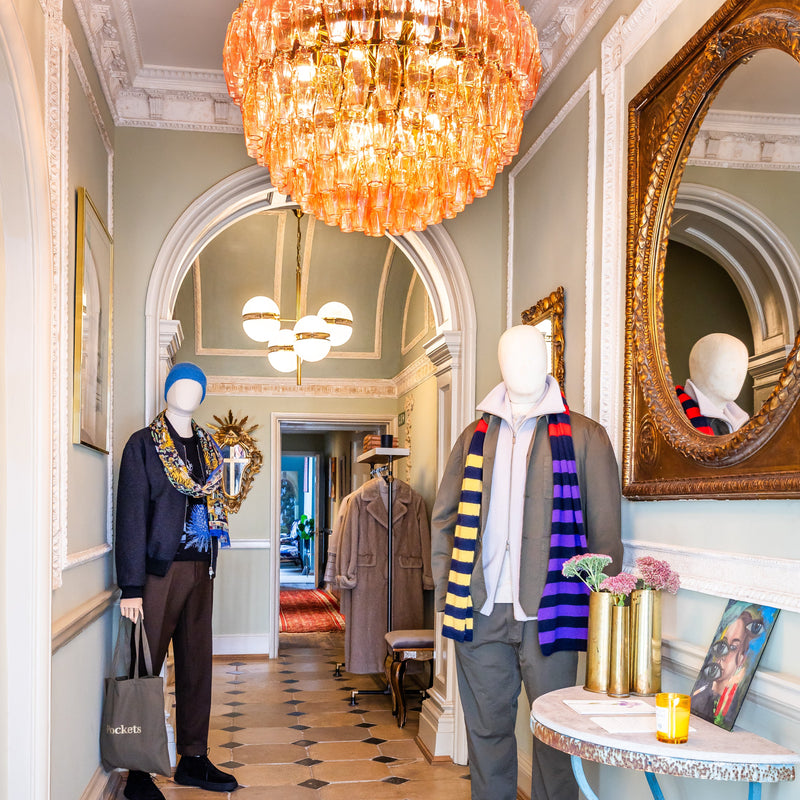 Interior of a stylish store with mannequins dressed in clothing, decorative mirrors, and a colorful chandelier.