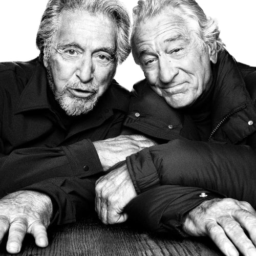 Two elderly men leaning on a textured surface, wearing matching dark jackets.