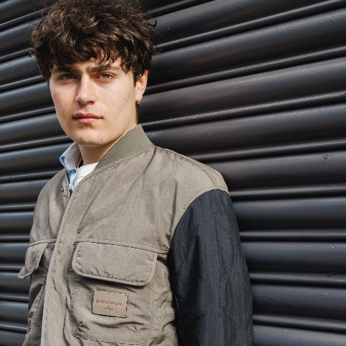 Man wearing a brown vest over a dark shirt against a metallic background