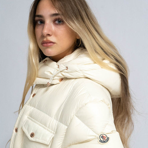 Woman wearing a cream-colored puffer jacket with a brand logo on a light gray background