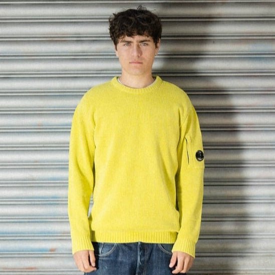 Person wearing a bright yellow sweater with a brand logo in front of a metallic shutter.