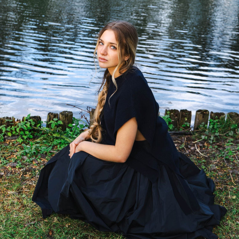 Woman in a black dress sitting by a body of water