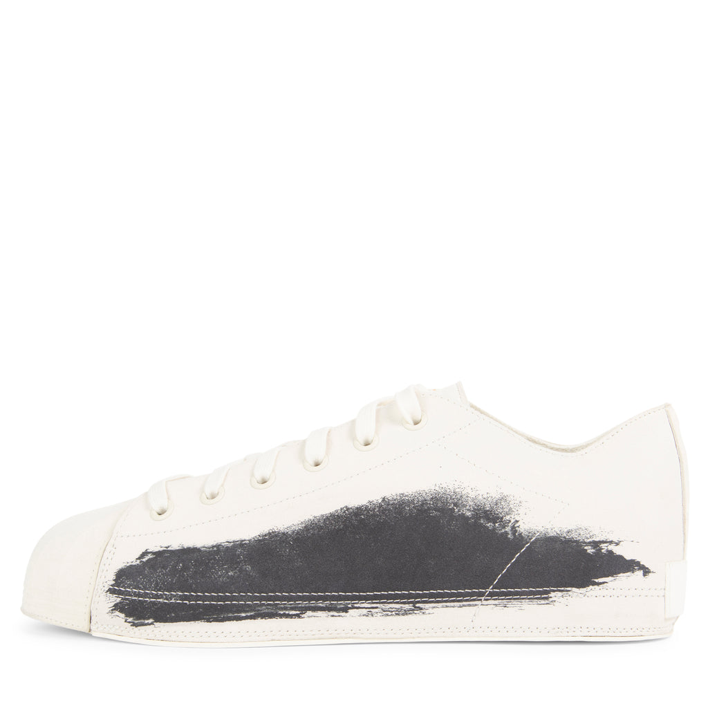 White sneaker with black paint splatter on a white background