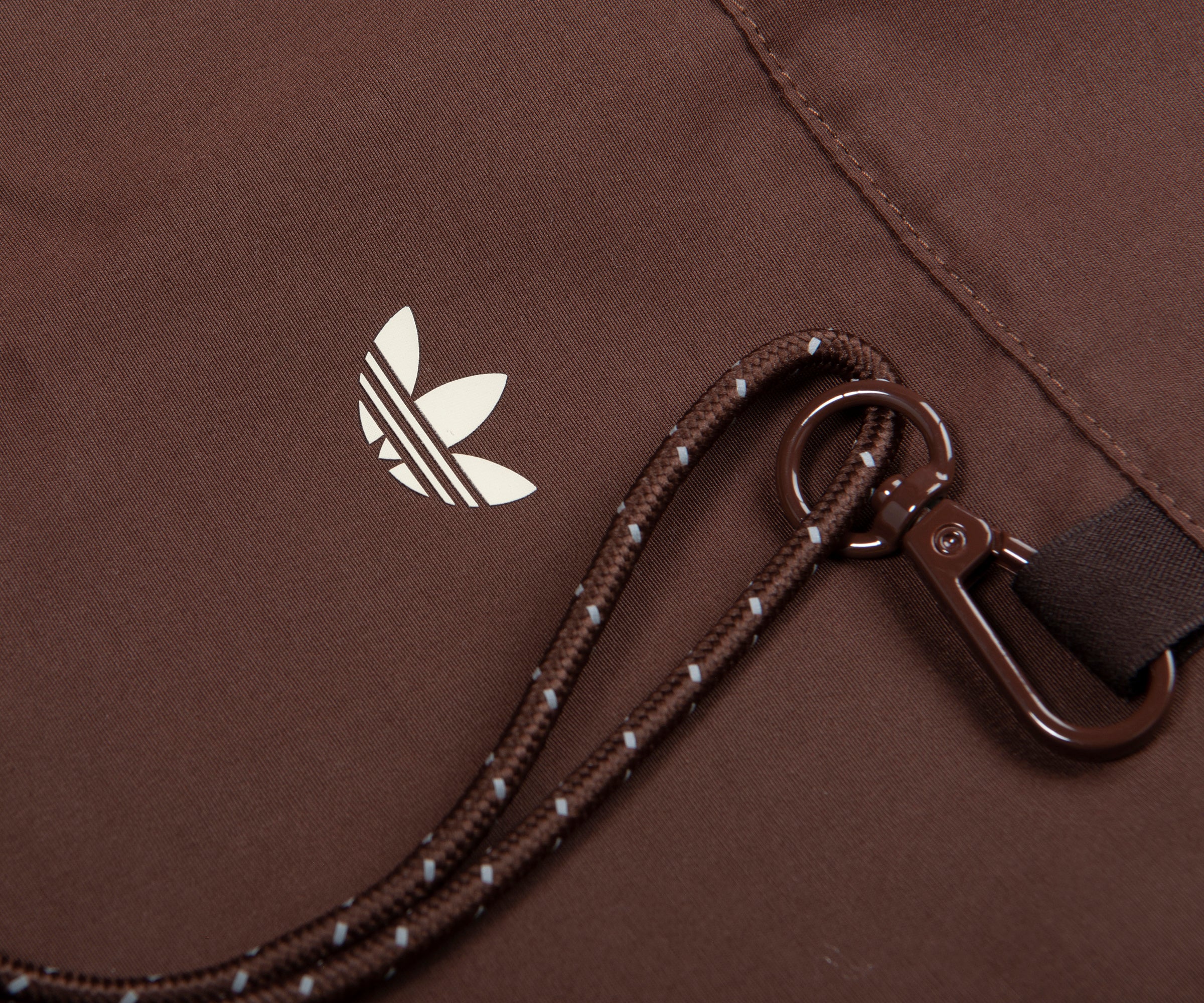 Close-up of a brown bag with an Adidas logo and strap.