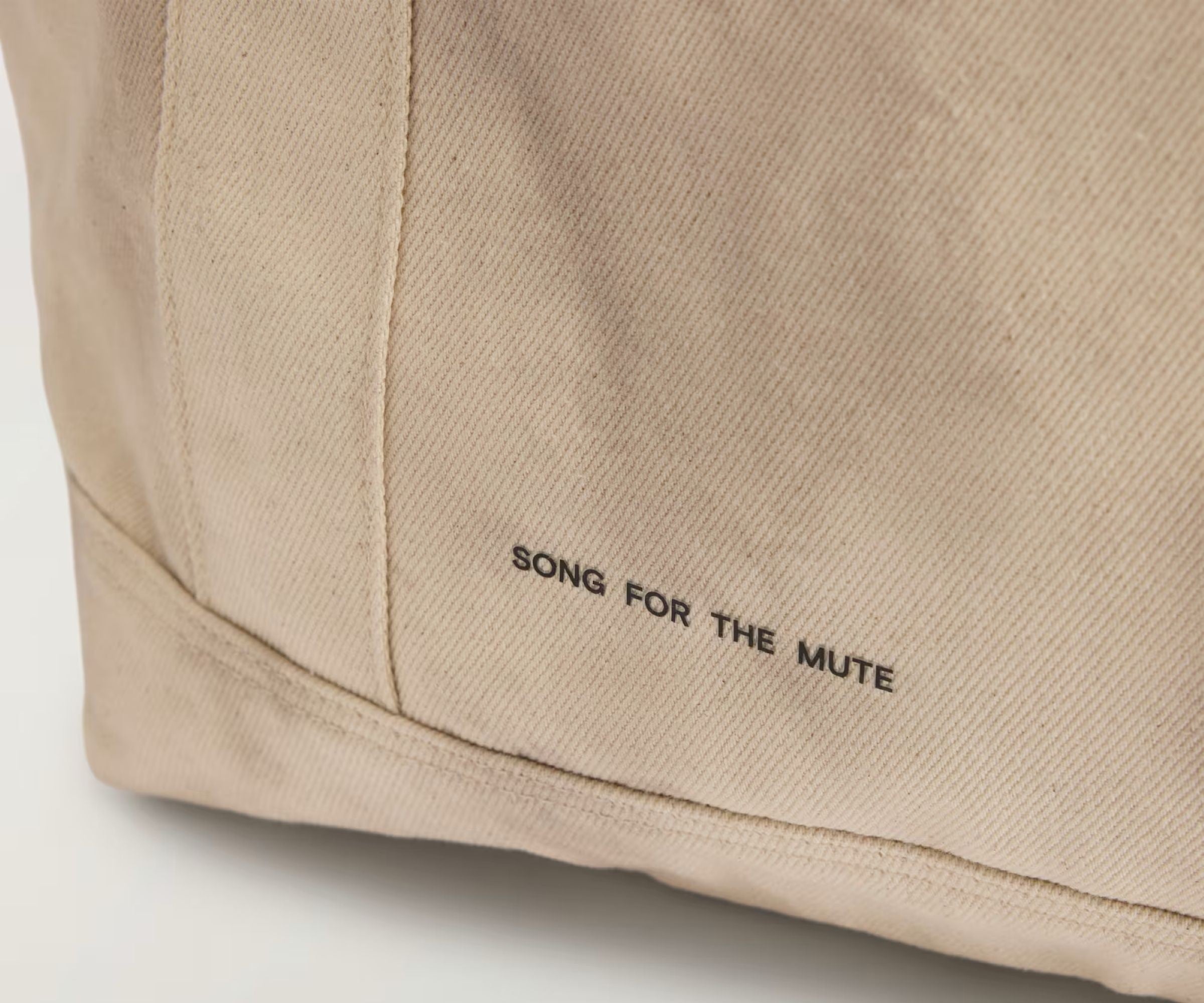 Beige fabric with 'SONG FOR THE MUTE' branding on a light gray background