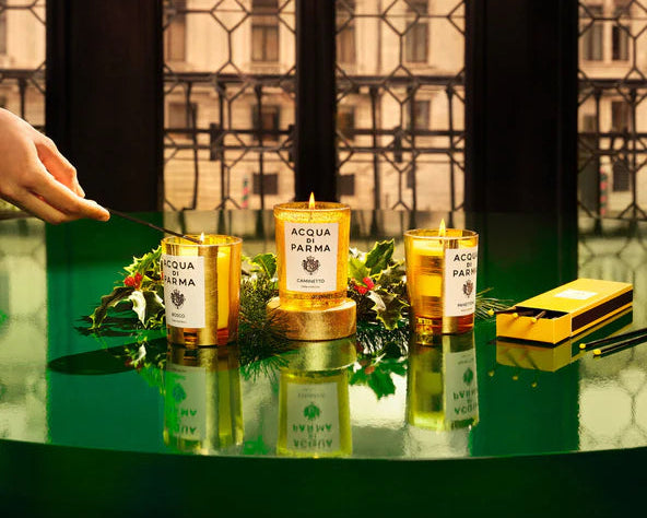Acqua di Parma candles on a reflective surface with a blurred background