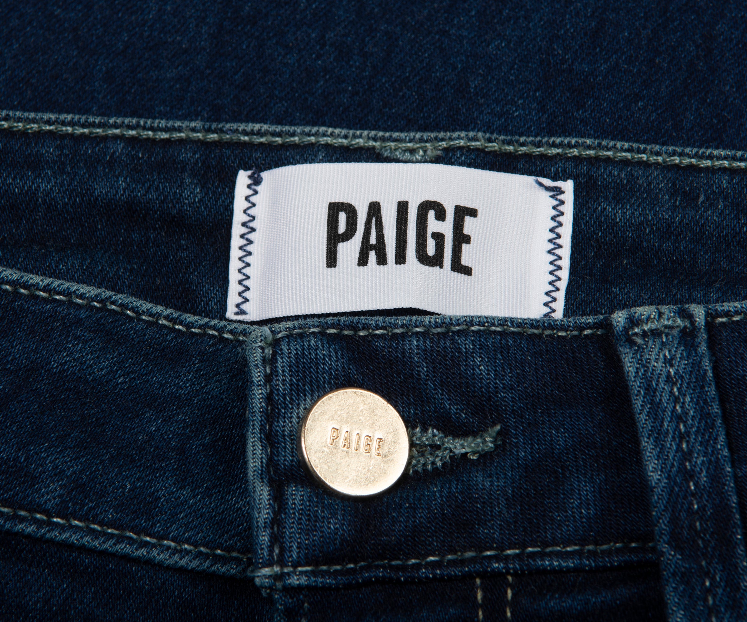 Close-up of Paige denim label on a dark blue fabric background