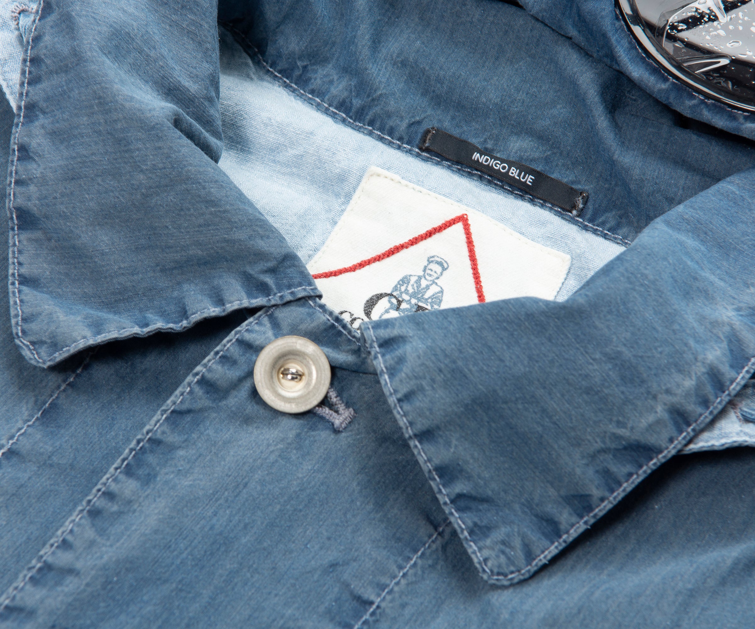 Close-up of a blue denim shirt with a button and label inside.