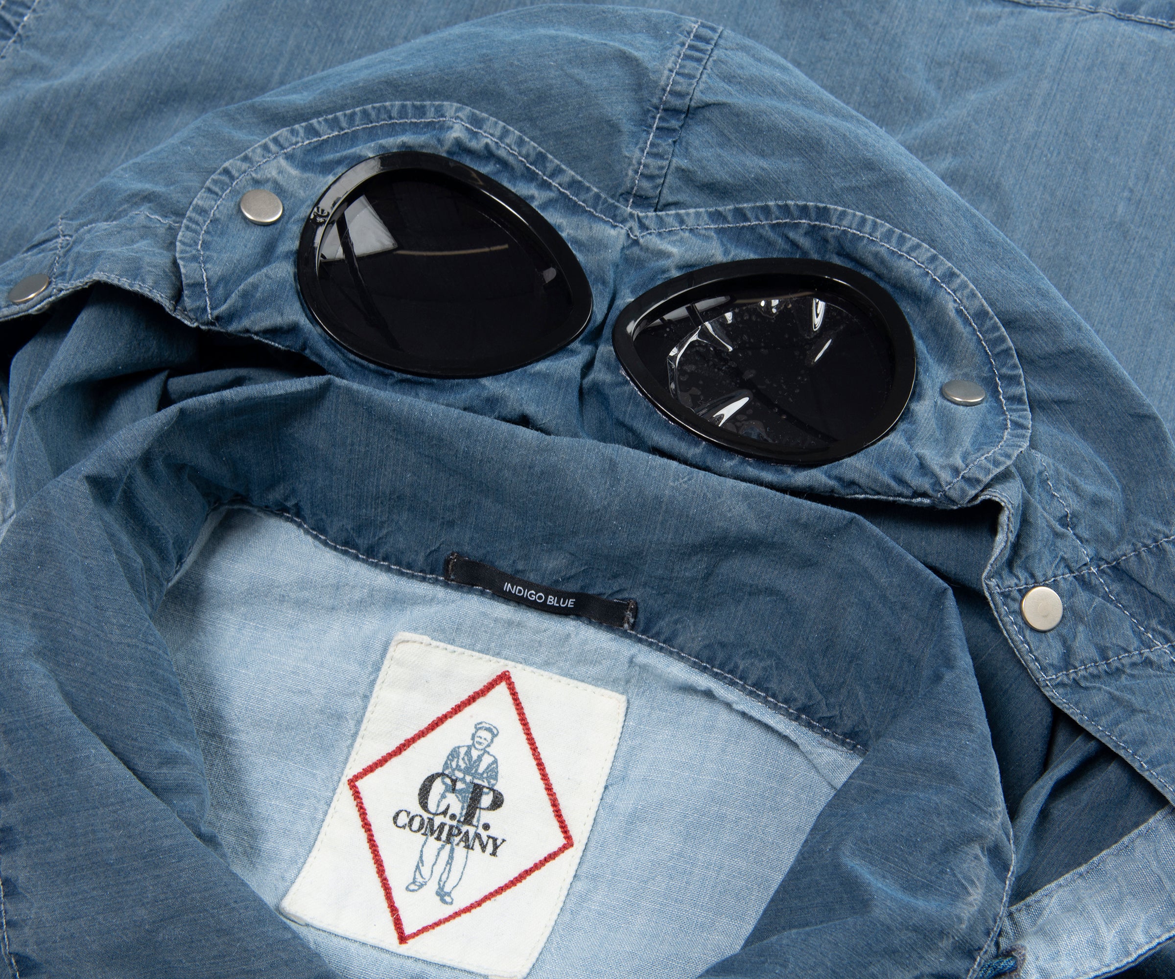 Blue denim jacket with goggle lenses and a brand label on a blurred background