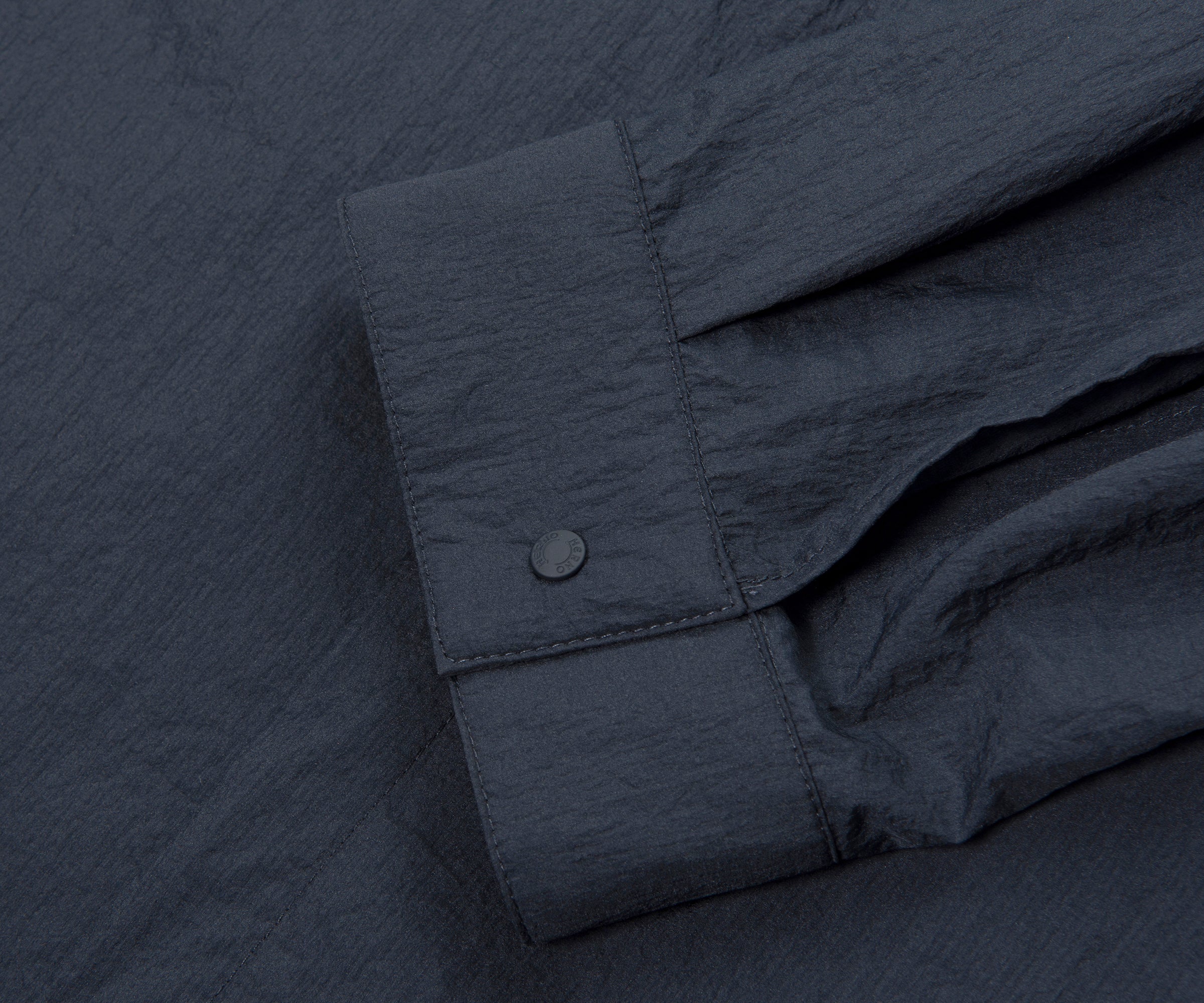 Close-up of a dark gray shirt with rolled-up sleeve on a matching fabric background