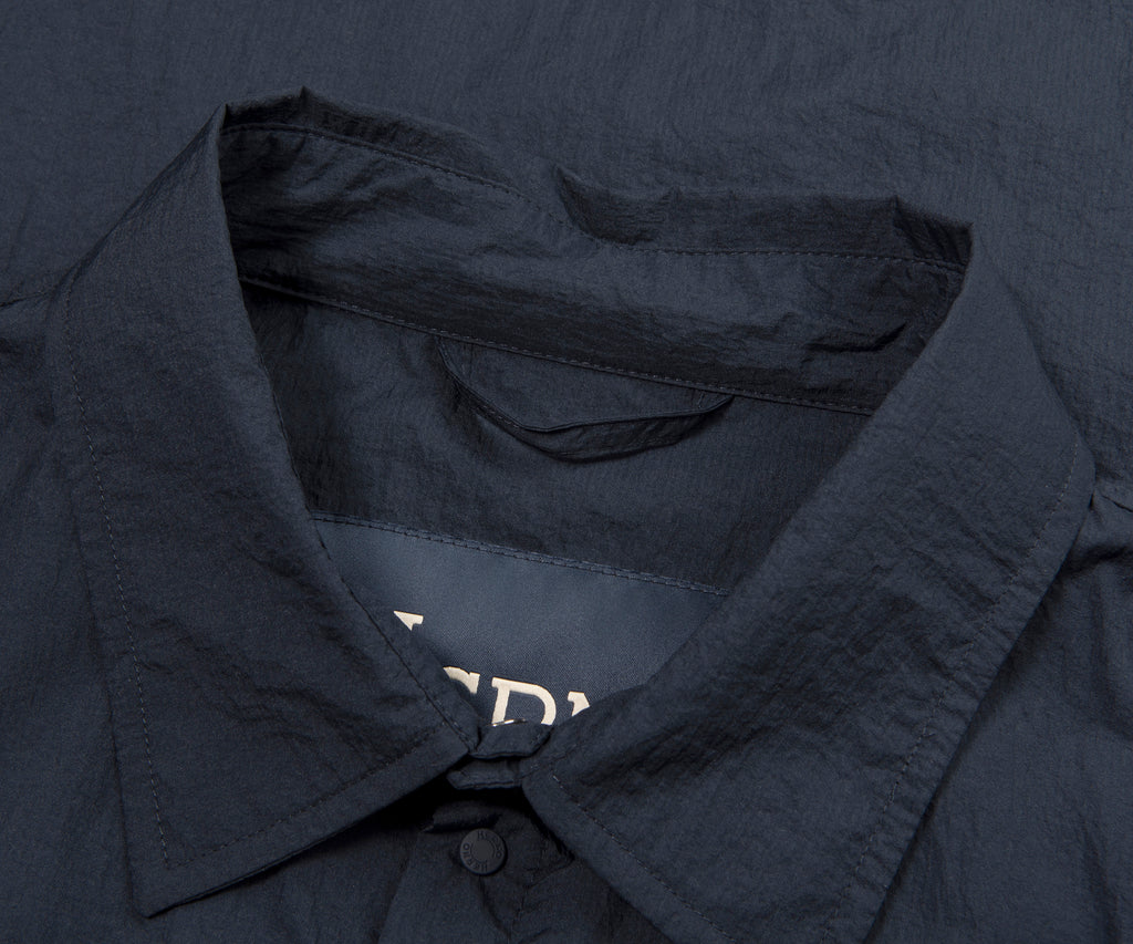 Close-up of a dark blue shirt with a collar and buttons, featuring the brand name 'Bella+Canvas'.