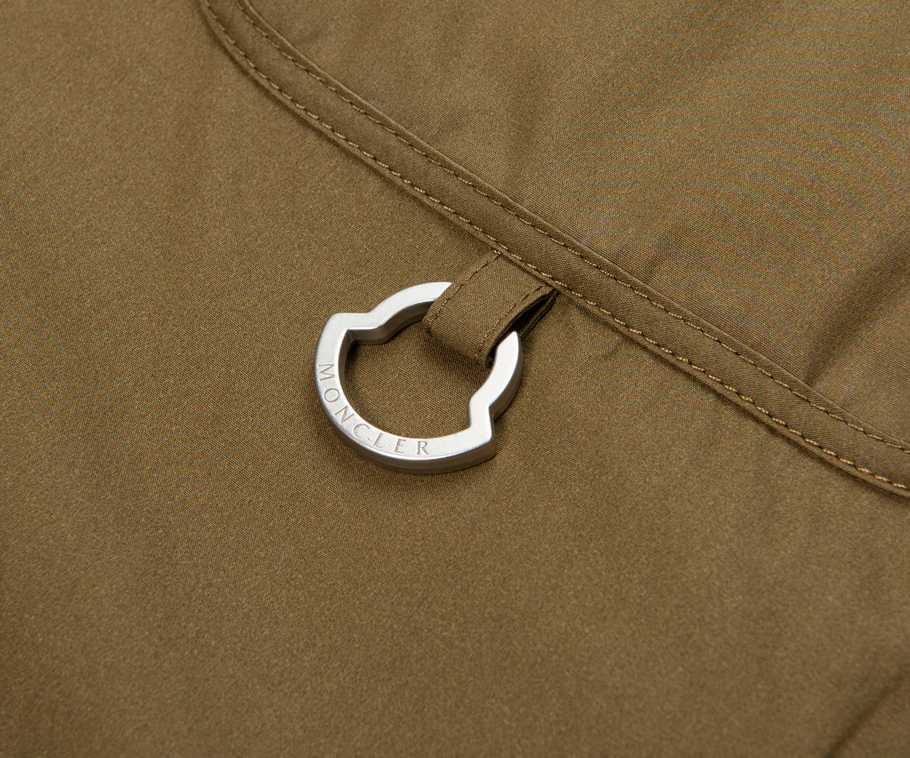 Close-up of a silver carabiner attached to a brown fabric surface.