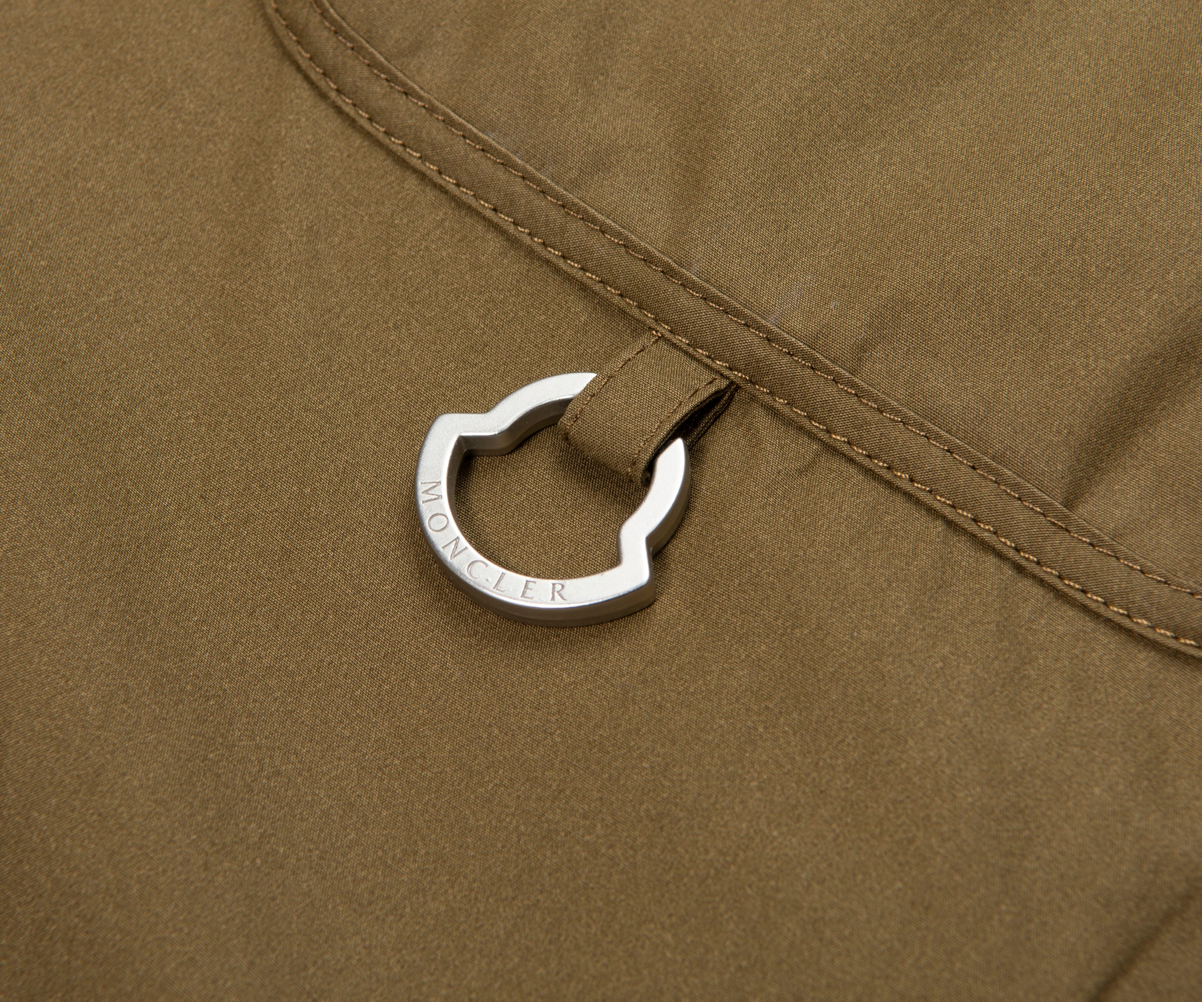 Close-up of a silver carabiner attached to a brown fabric surface.