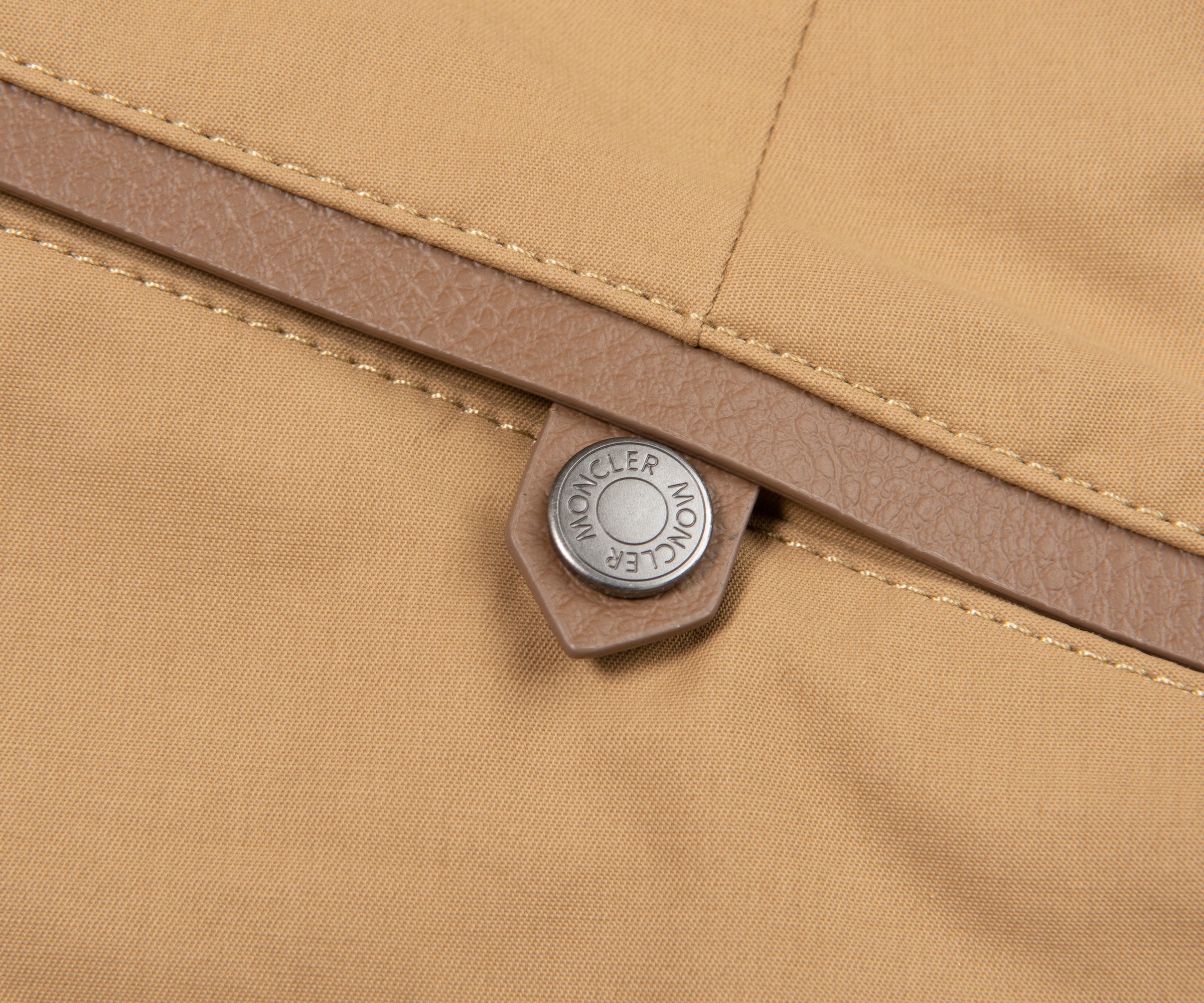 Close-up of a beige fabric with a brand label on a brown zipper.