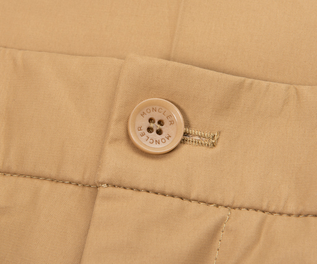 Close-up of a beige fabric with a button and zipper, featuring the Moncler brand logo.