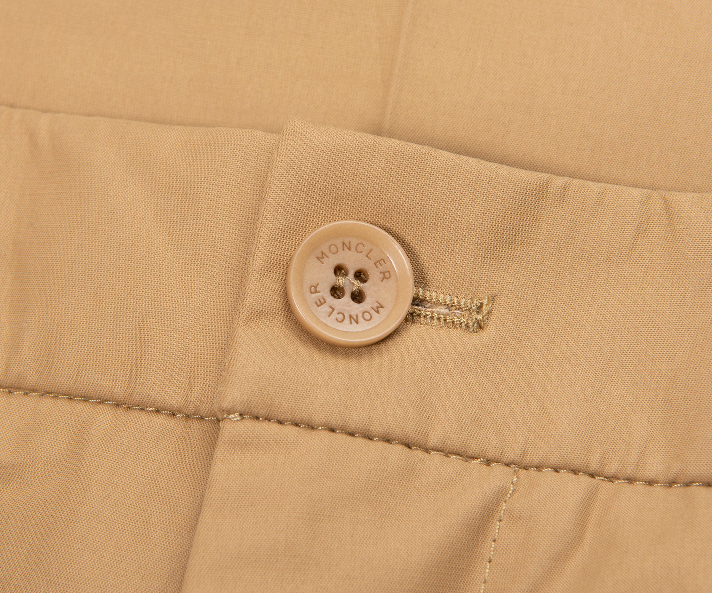 Close-up of a beige fabric with a button and zipper, featuring the Moncler brand logo.