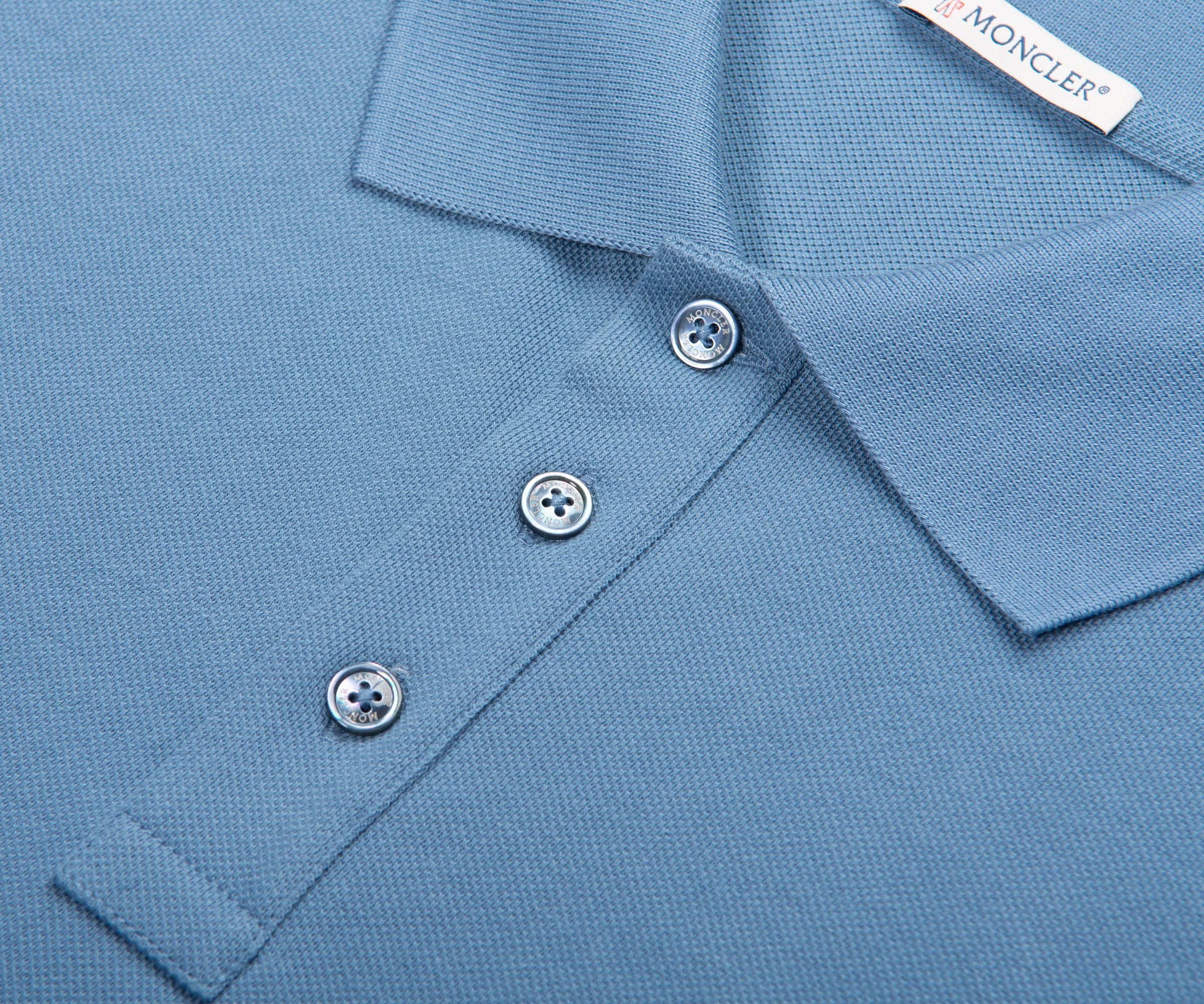 Close-up of a blue polo shirt with buttons and a Moncler label.