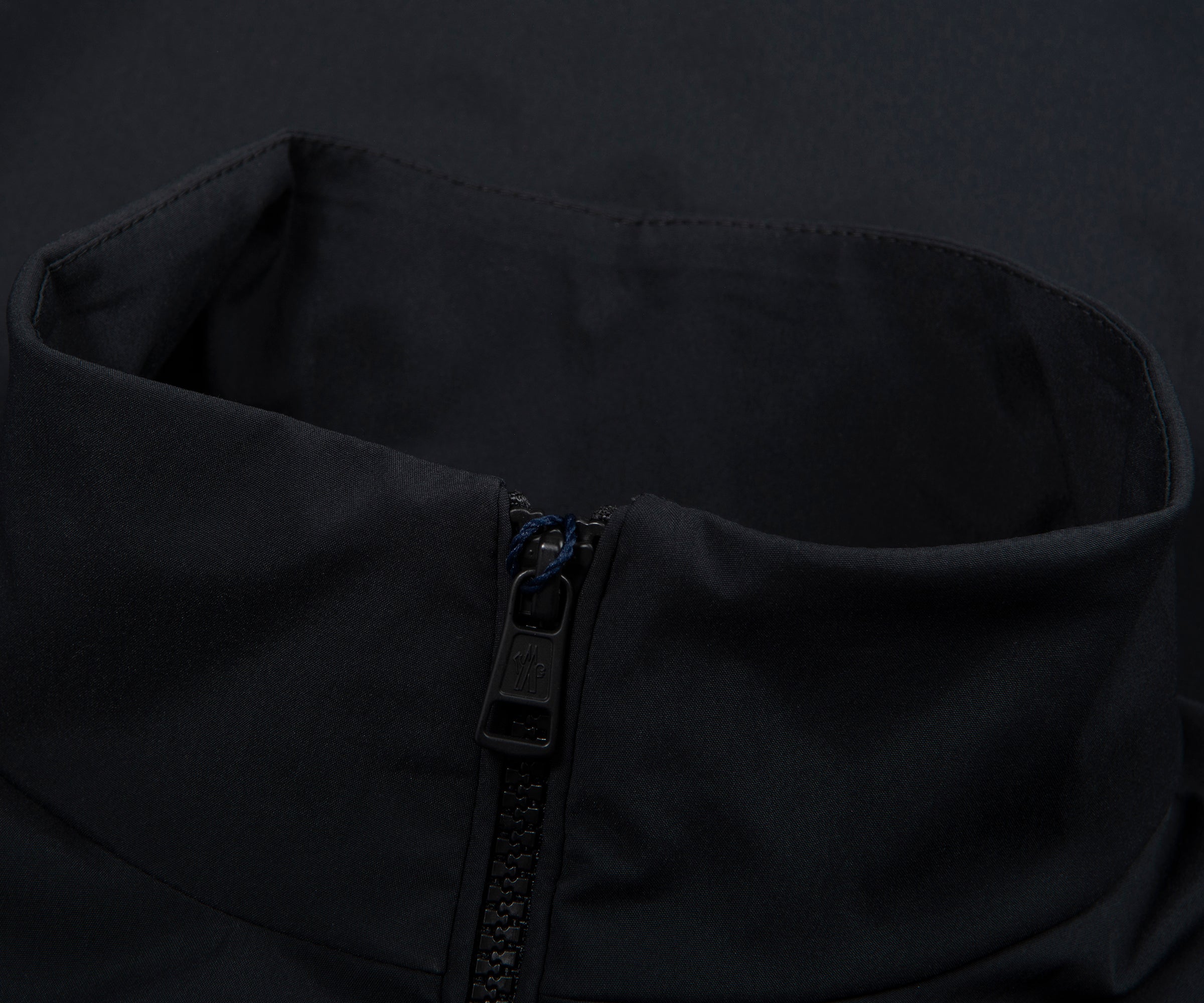 Close-up of a black jacket with a zipper and button details on a dark background