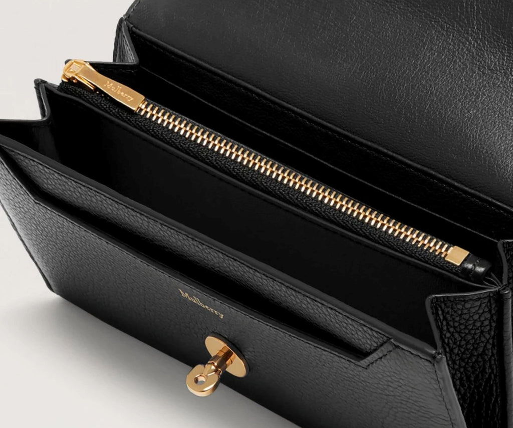 Black handbag with gold zipper and clasp on a light gray background