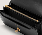 Black handbag with gold zipper and clasp on a light gray background