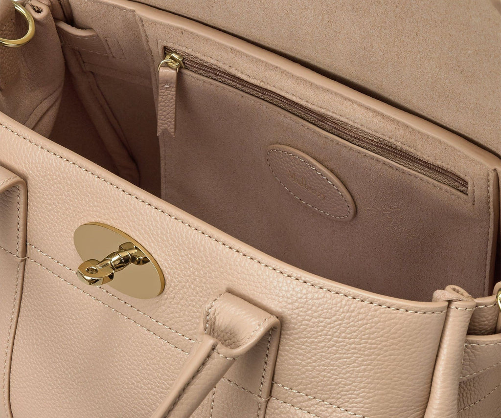 Close-up of a beige handbag with a gold lock and interior pocket.