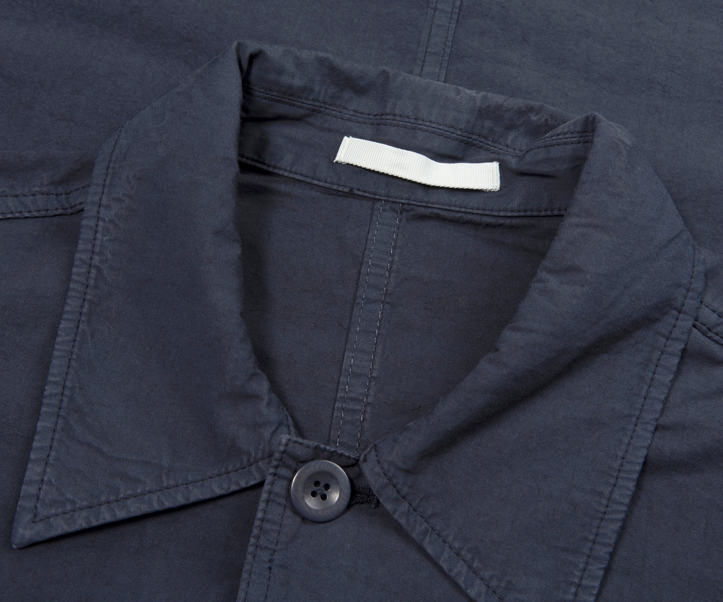 Close-up of a navy blue shirt collar with a button and a brand label.
