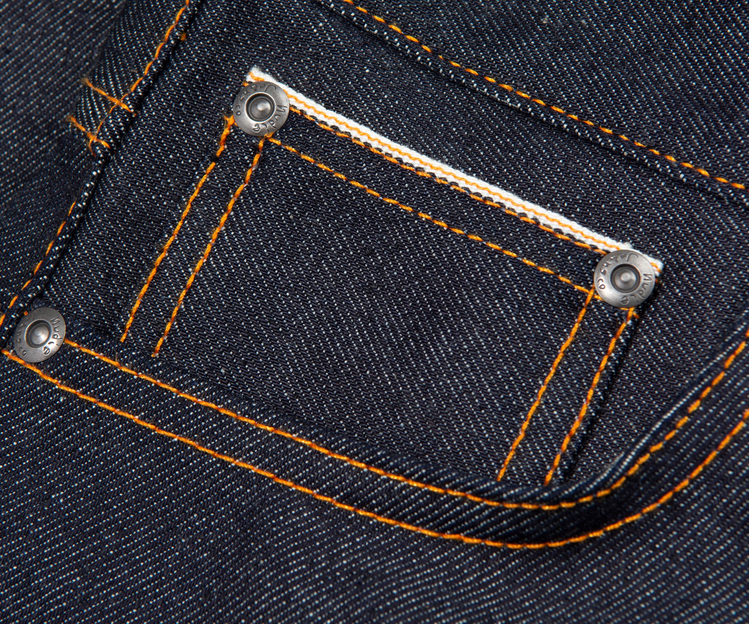 Close-up of a pocket on a pair of dark blue jeans with orange stitching.