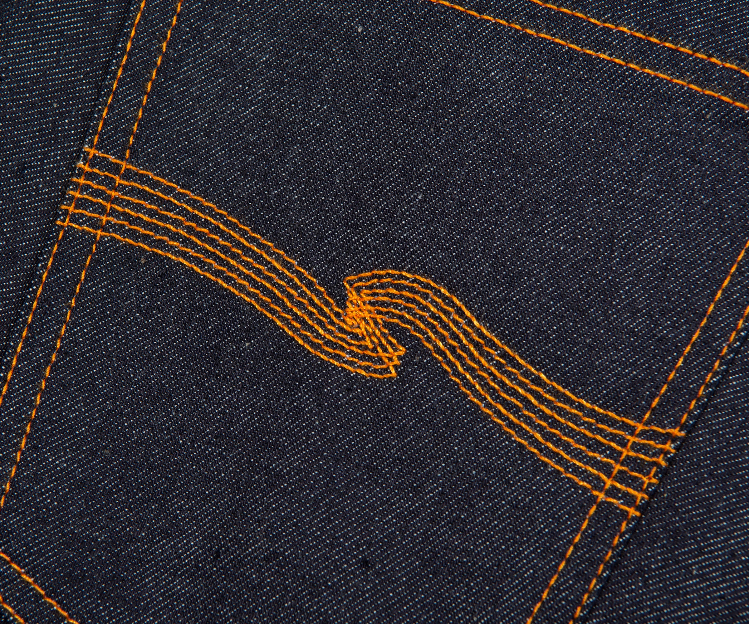Close-up of dark denim fabric with orange stitching forming a pattern.