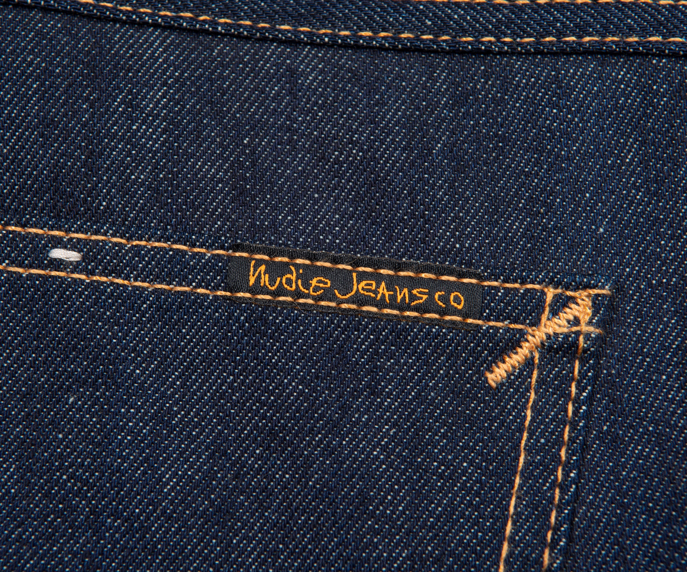 Close-up of a blue denim fabric with 'Nude Jeans Co.' branding.