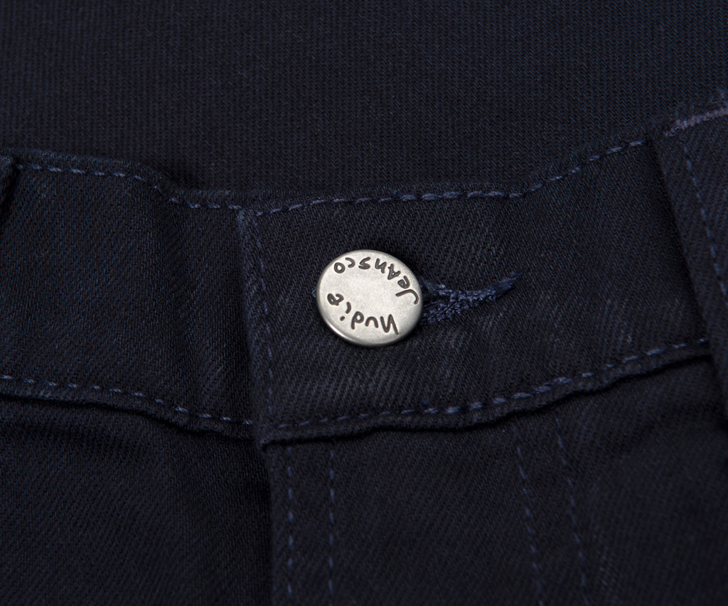 Close-up of a button on a dark fabric, likely jeans, with 'Nudie Jeans' branding.