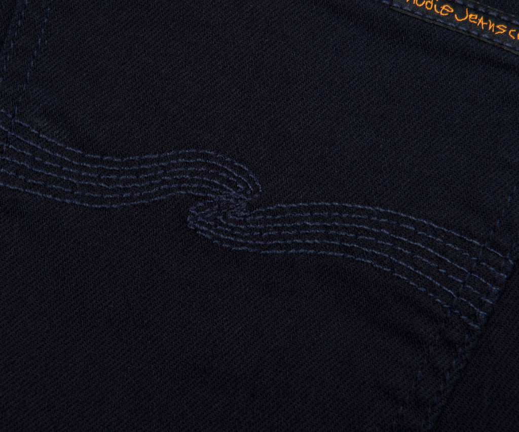 Close-up of a black fabric with embroidered design and 'Nudie Jeans' branding.