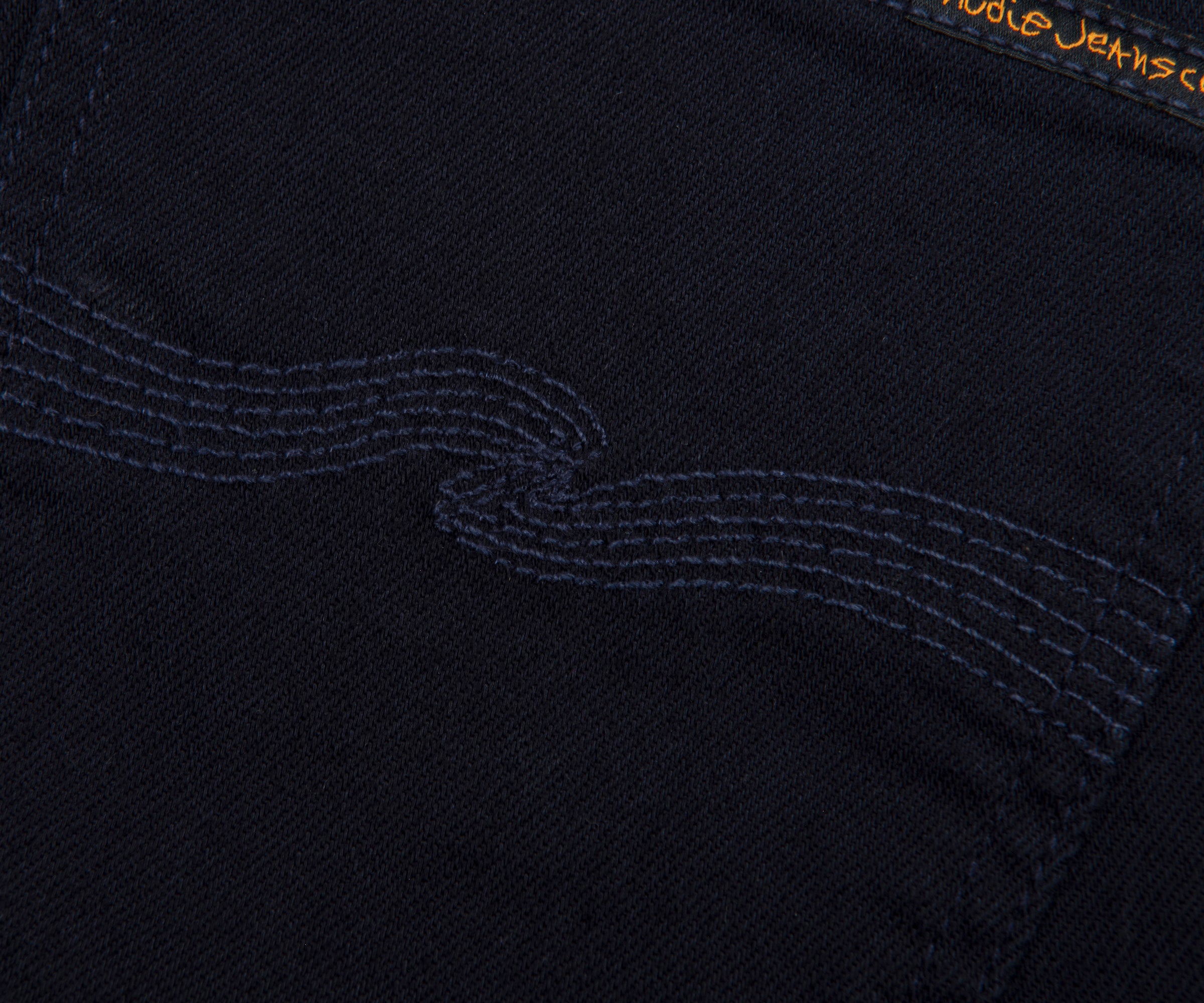 Close-up of a black fabric with embroidered design and 'Nudie Jeans' branding.