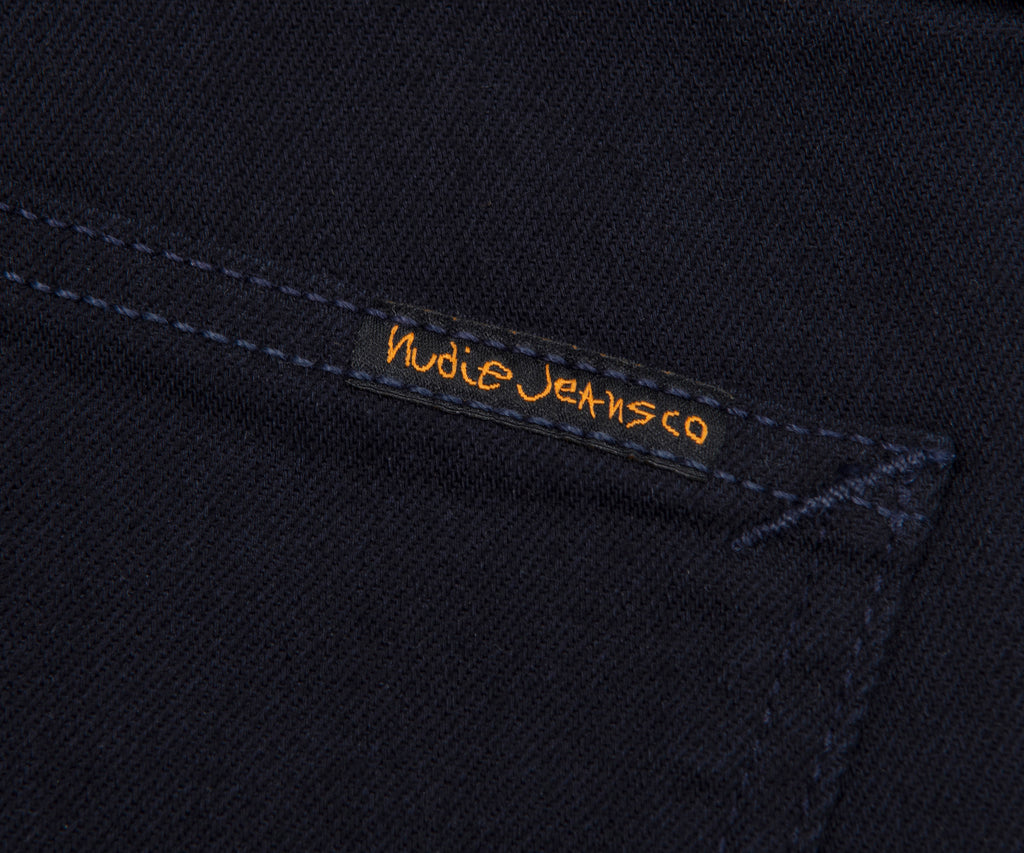 Nudie Jeans logo on a dark fabric background