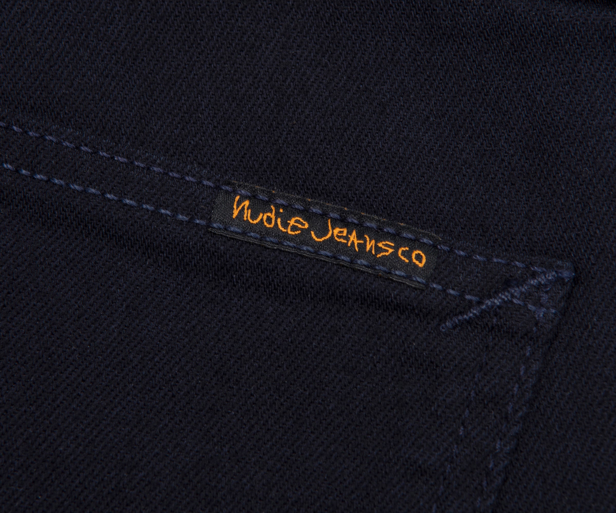 Nudie Jeans logo on a dark fabric background