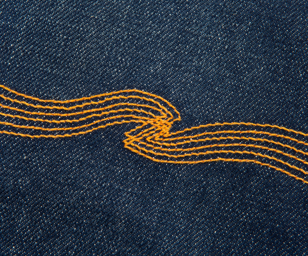 Close-up of blue denim fabric with yellow stitching