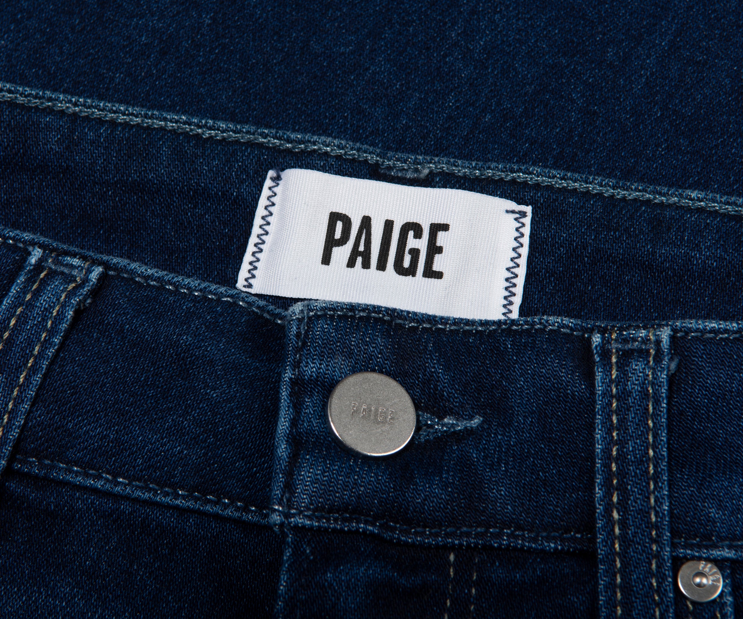 Close-up of a Paige denim label on a blue denim fabric.