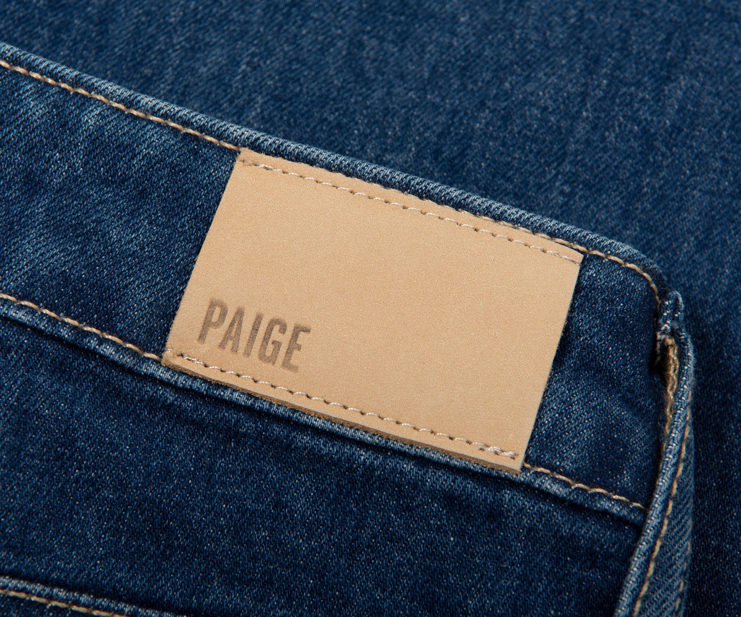 Close-up of a Paige denim label on blue denim fabric.