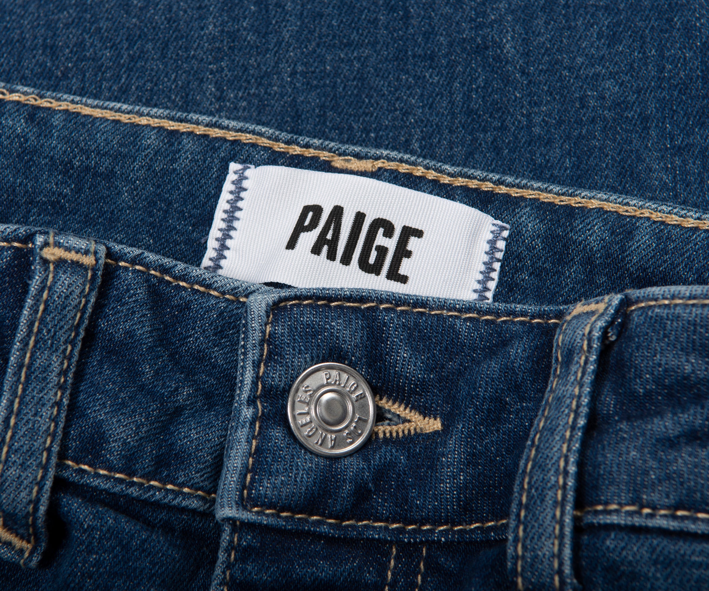 Close-up of a Paige denim label on a blue denim fabric.