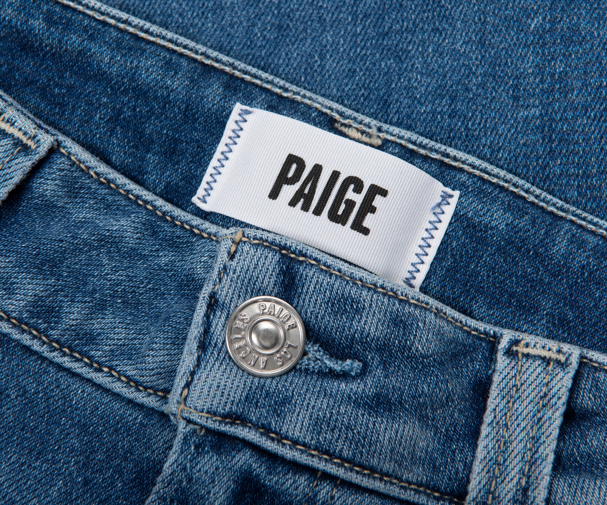 Close-up of a Paige denim label on a blue denim fabric.