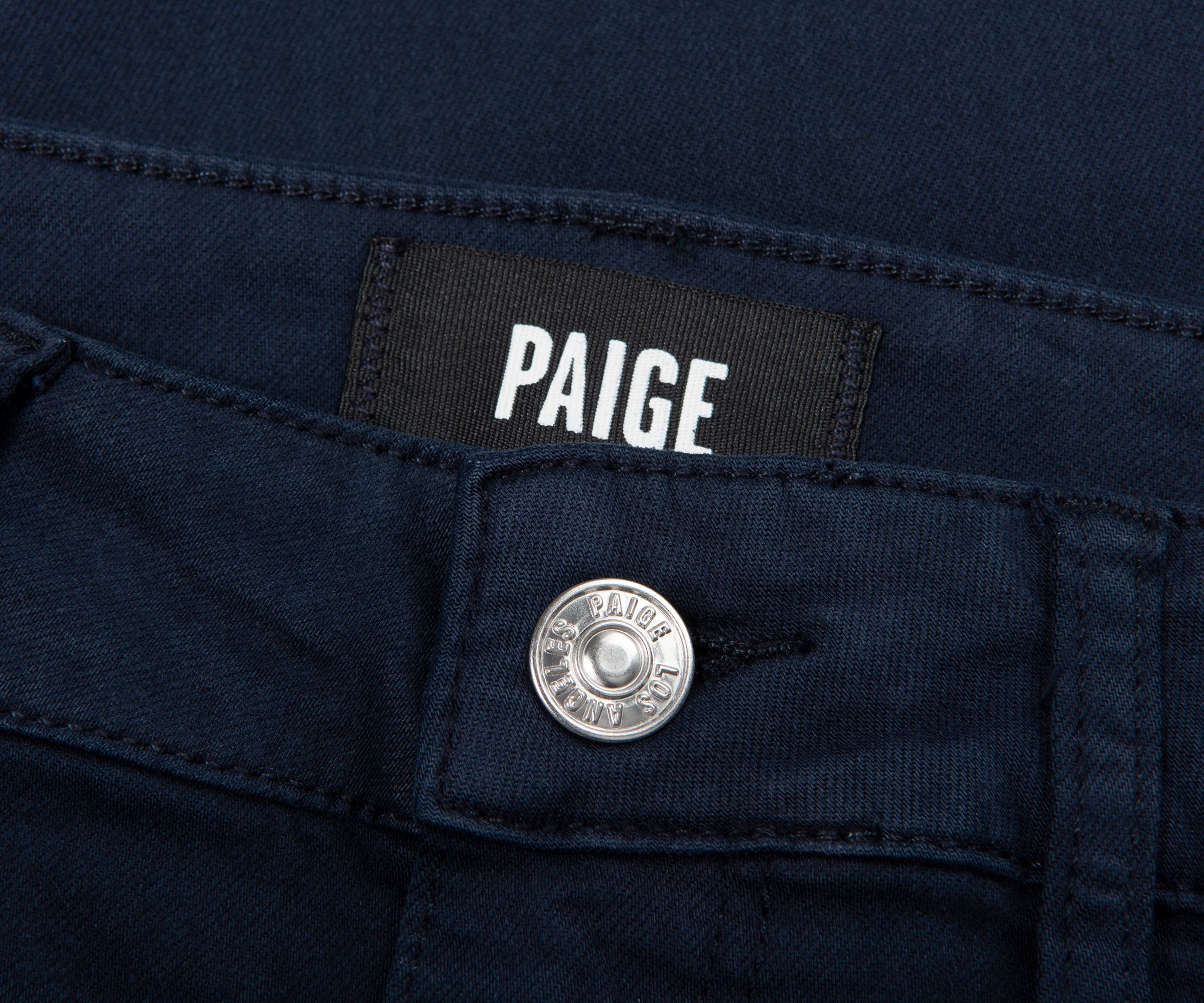 Close-up of a navy blue jeans pocket with 'Paige' brand label and button.