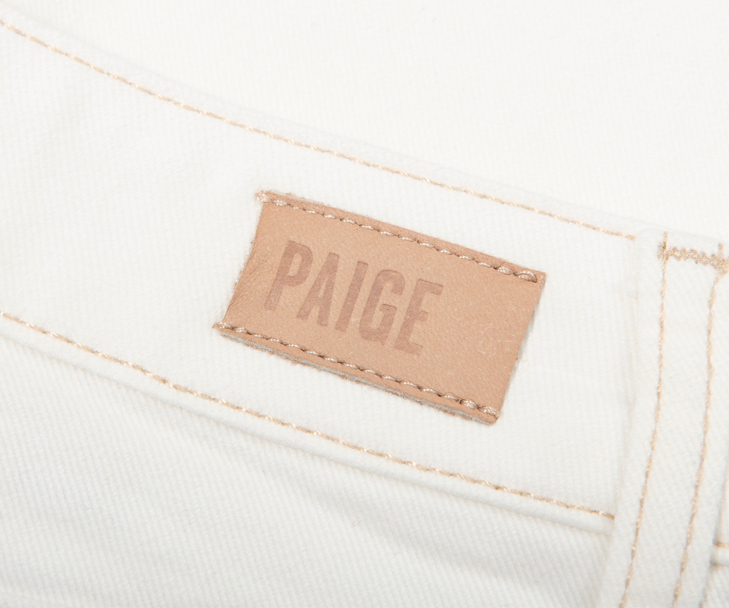 Close-up of a 'Paige' label on white denim fabric.
