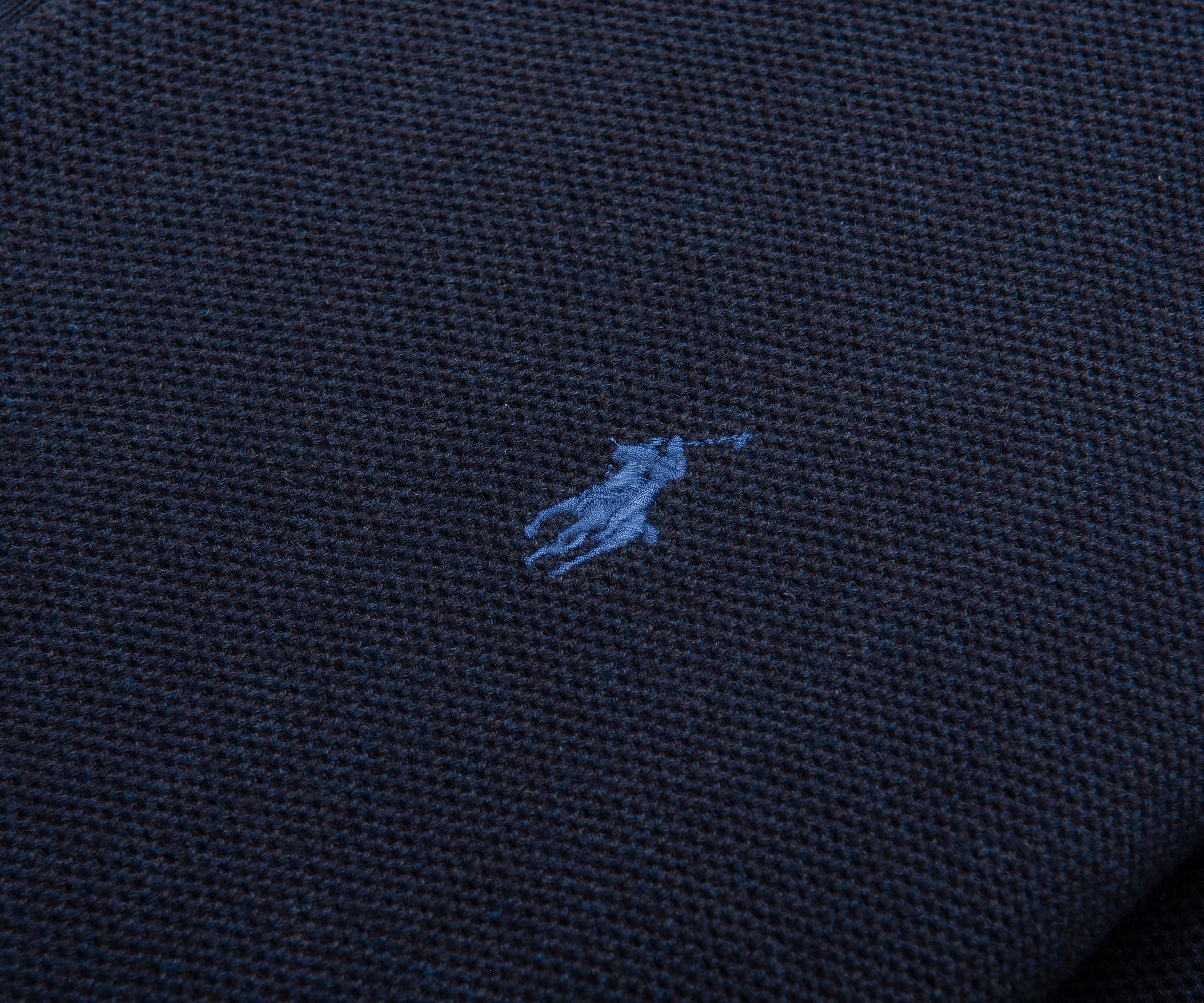 Close-up of a dark blue fabric with a small embroidered logo.