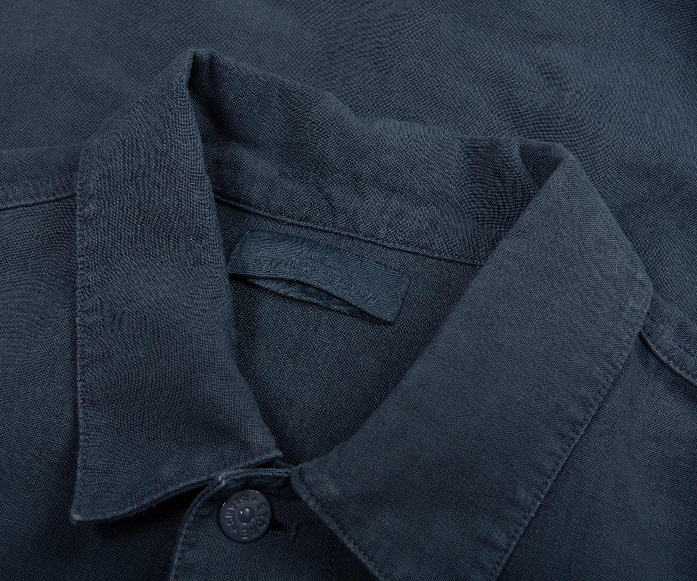 Close-up of a dark blue shirt collar with a button on a matching fabric background