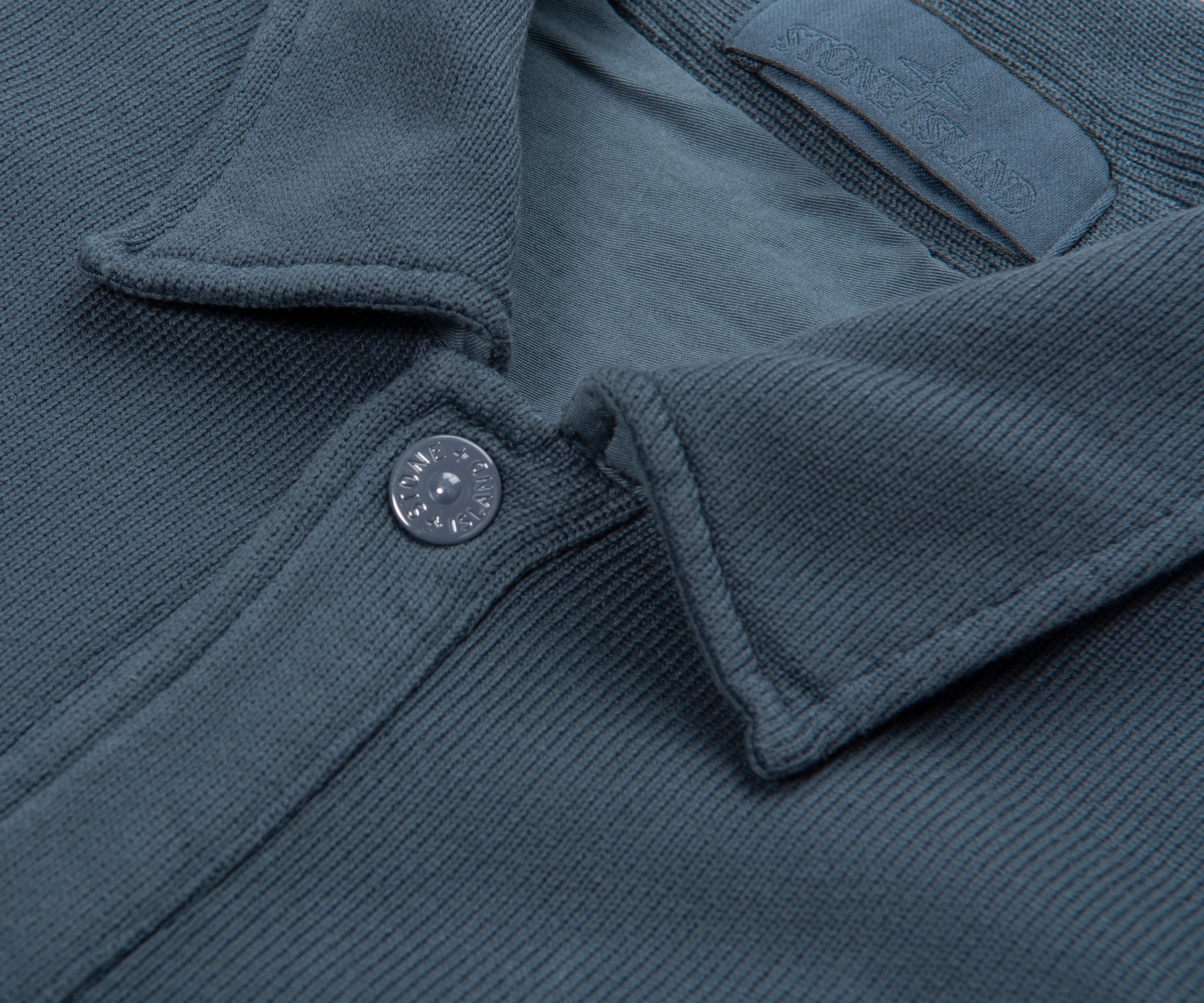 Close-up of a dark gray jacket with a button on a matching fabric background