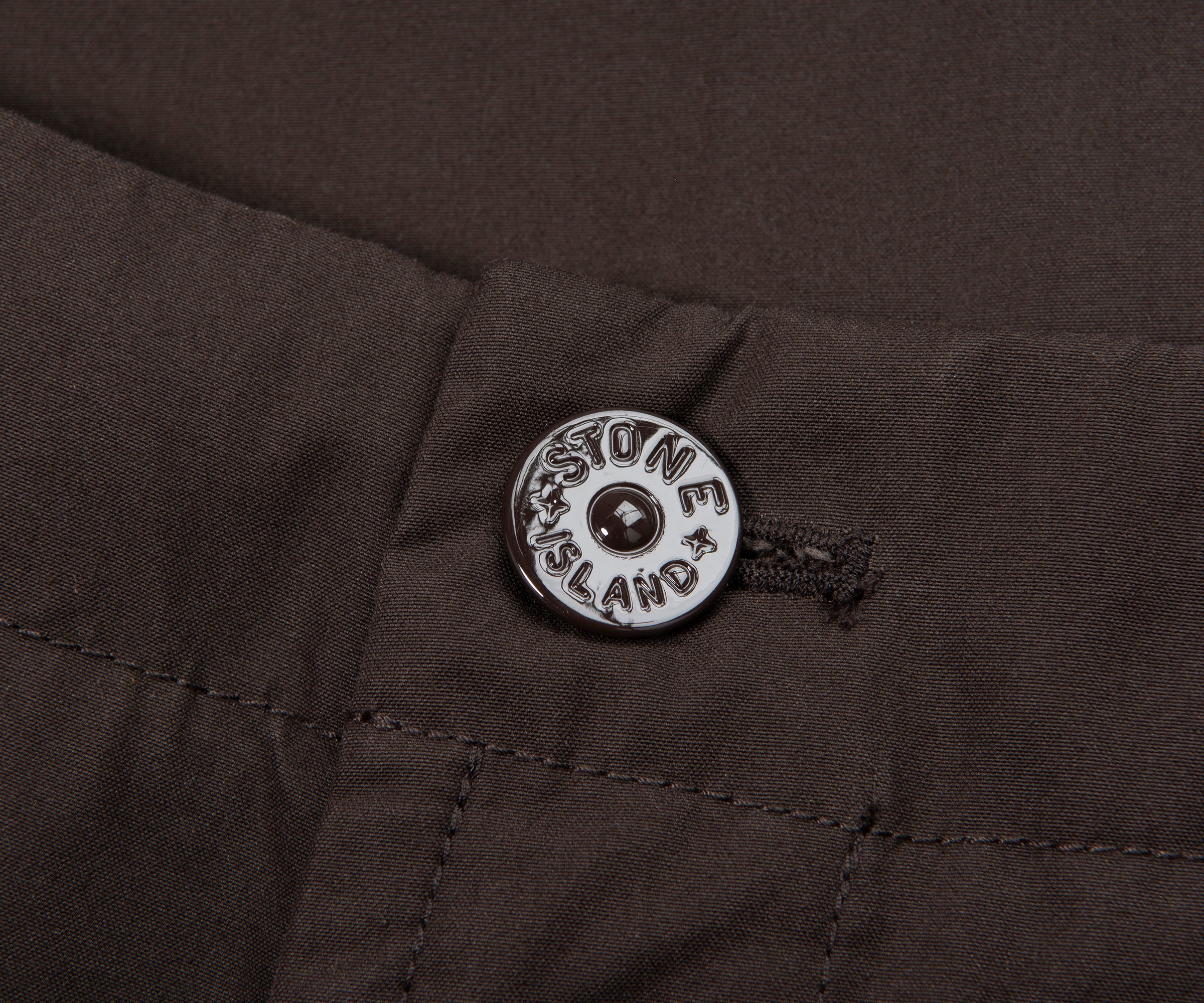 Close-up of a button on a dark fabric with 'Massone Island' branding.
