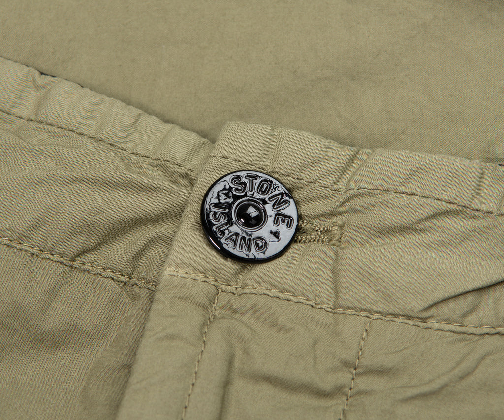 Close-up of a button on a green fabric with 'Stone Island' branding.