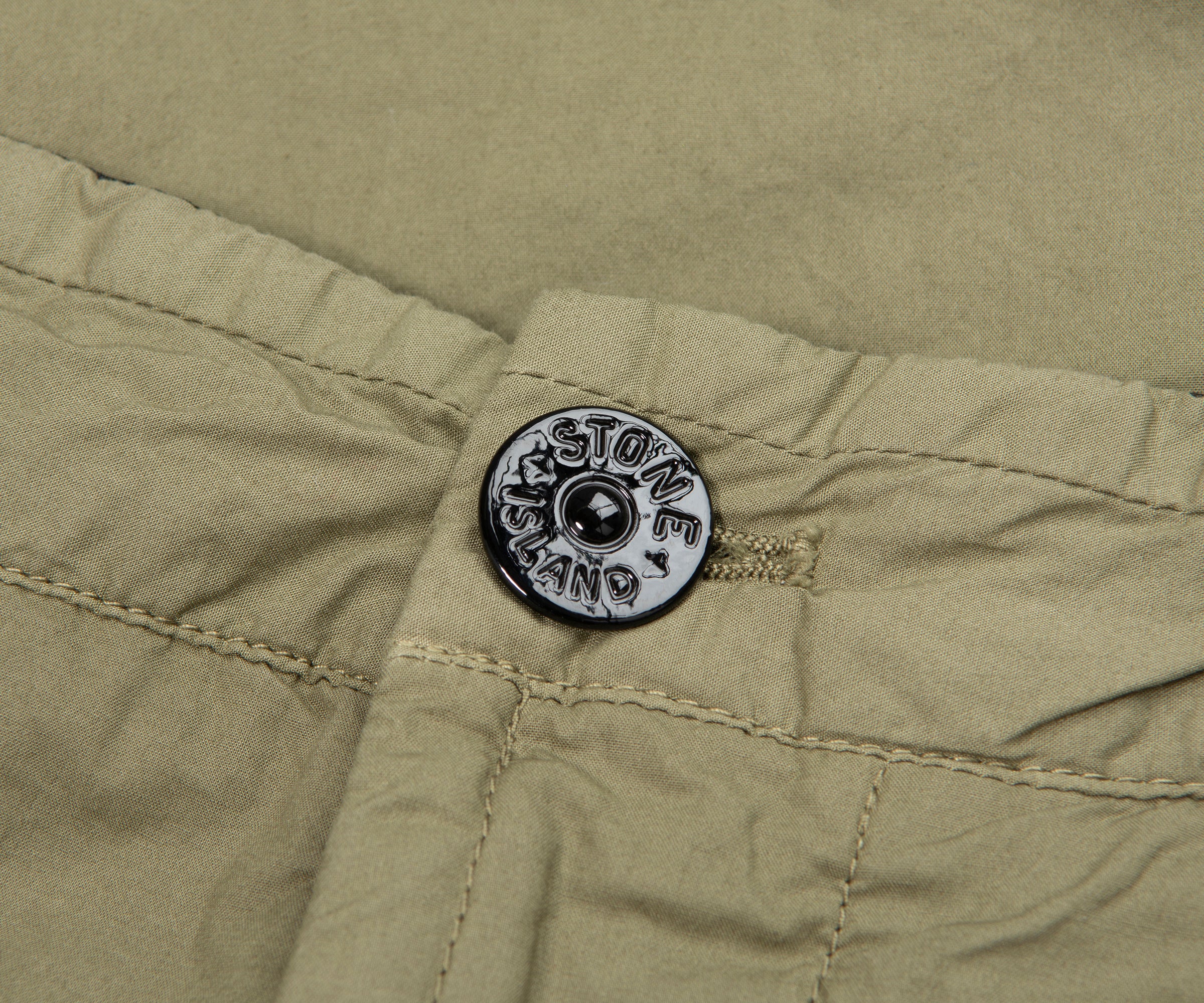 Close-up of a button on a green fabric with 'Stone Island' branding.