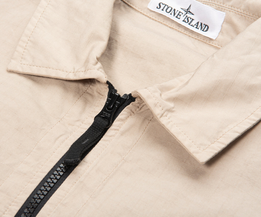 Close-up of a beige jacket with a black zipper and Stone Island label.