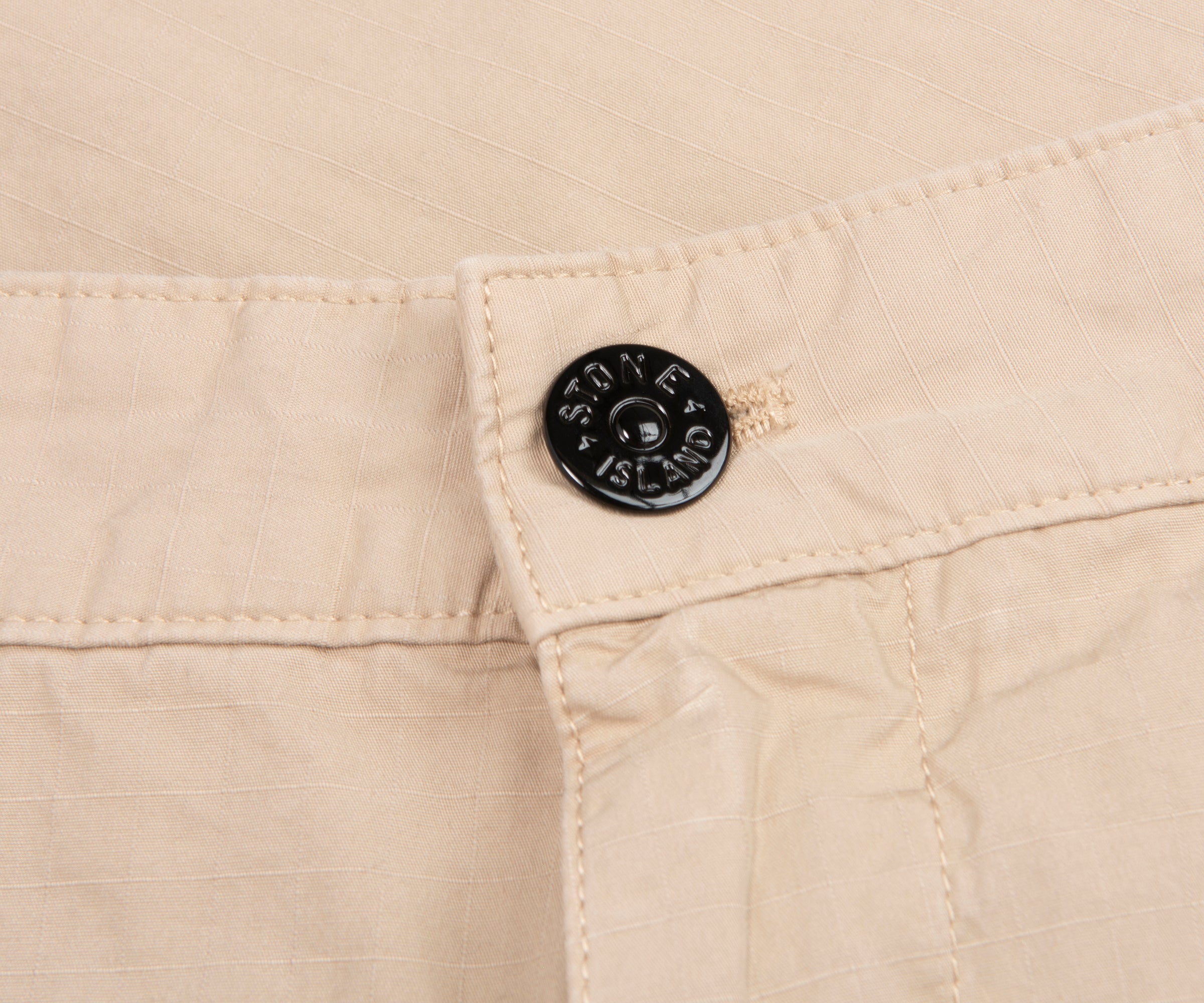Close-up of beige fabric with a button featuring a logo.