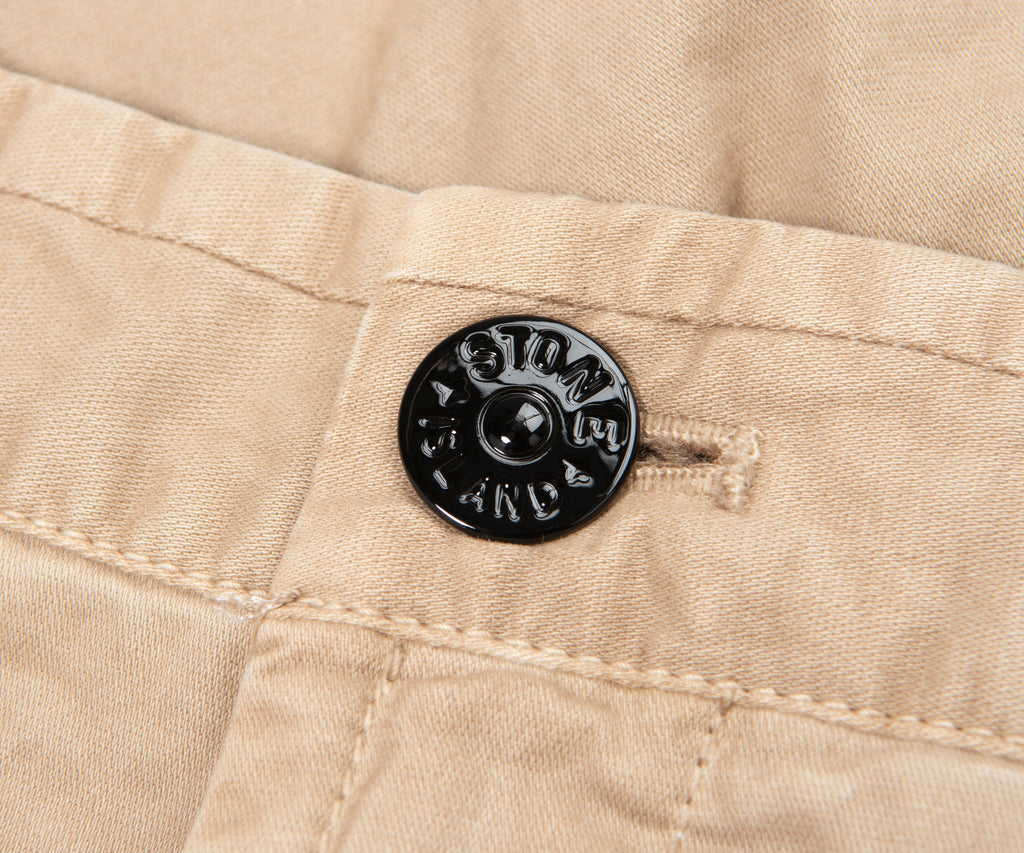 Close-up of a beige fabric with a black button featuring 'Stone Island' branding.